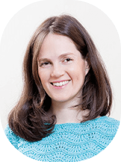 אדם מחייך עם שיער חום עד הכתפיים לבוש טופ בעל מרקם תכלת, צולם על רקע רגיל.