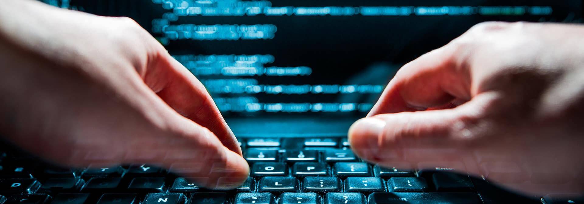 Close-up of a יד אנושית typing on a keyboard, with a computer screen displaying lines of code in the background. The focus is on the rapid movement of the fingers, suggesting fast typing or coding activity.