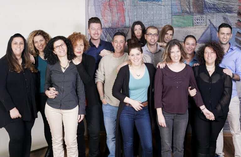 קבוצה של שלושה עשר אנשים, כולל חברי חבר תרגומים, עומדים צמוד זה לזה, מחייכים למצלמה. הם נמצאים בתוך הבית עם ציור מופשט צבעוני על הקיר מאחוריהם. הקבוצה מורכבת מגברים ונשים כאחד, לבושים בלבוש יומיומי.