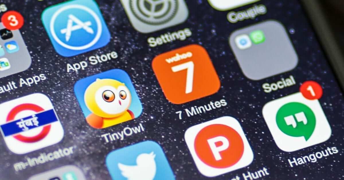 תקריב של מסך סמארטפון המציג סמלי אפליקציות שונים כמו App Store, Settings, TinyOwl עם גרפיקת הינשוף שלו, 7 דקות ו-Hangouts עם תג התראה. הרקע המכוכב מדגיש את הלוקליזציה המקצועית המושגת על ידי שימוש בכלים הנכונים.