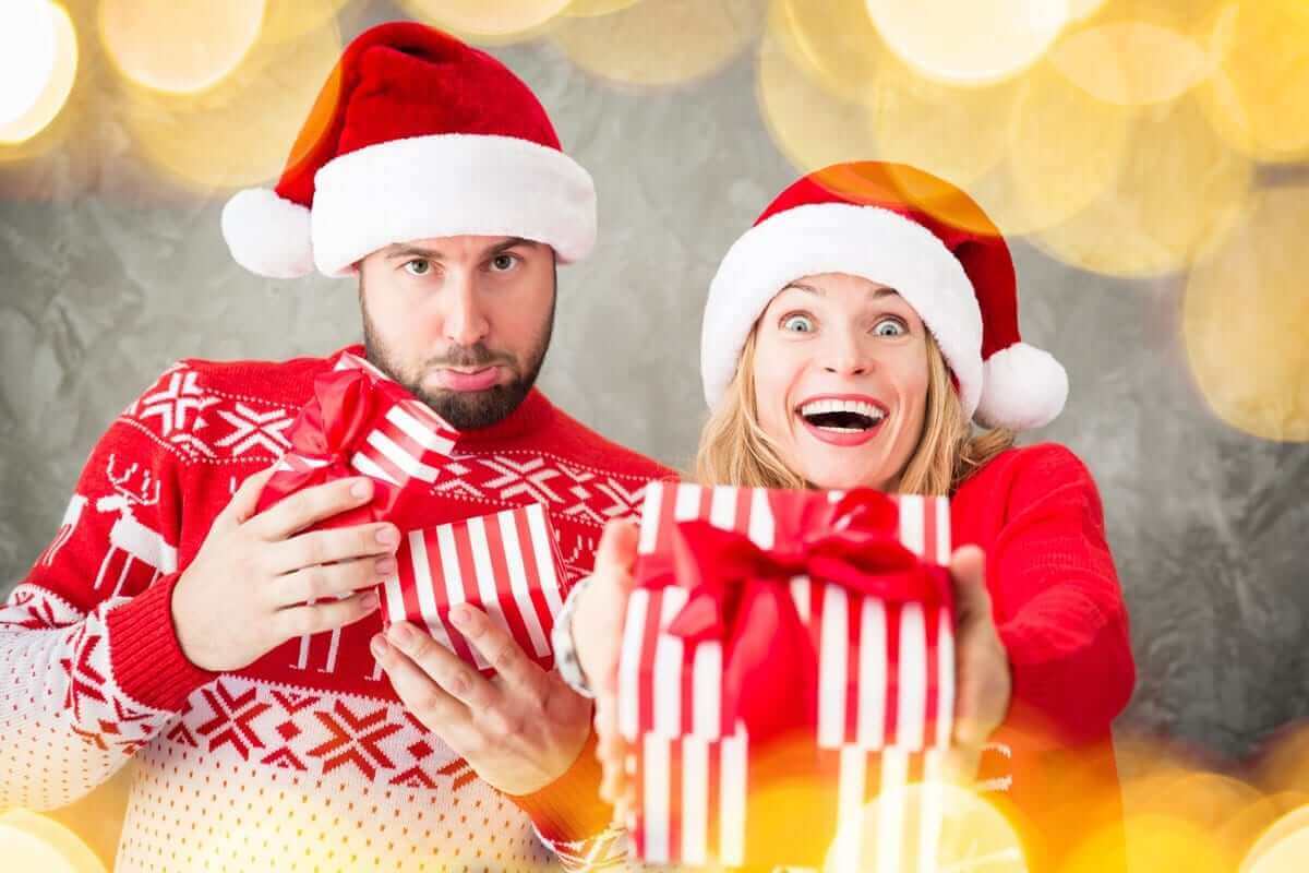 גבר ואישה עם כובעי סנטה וסוודרים אדומים אוחזים בקופסאות מתנה מפוספסות. הגבר נראה מופתע עם קופסה פתוחה, בעוד האישה, מחייכת חיוך רחב, מושיטה קופסה סגורה לכיוון המצלמה - לוכדת את השמחה של דצמבר 2018 בין אורות חמים ומטושטשים.