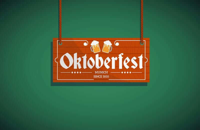 על שלט עץ על רקע ירוק כתוב אוקטוברפסט באותיות לבנות מודגשות, כששני ספלי בירה מוקצפים מצלצלים מעל הטקסט. למטה, הוא מציין את מינכן מאז 1810. השלט תלוי בשני חבלים, מהדהד את הרוח החגיגית המזכירה את חגיגות אוקטובר 2018.