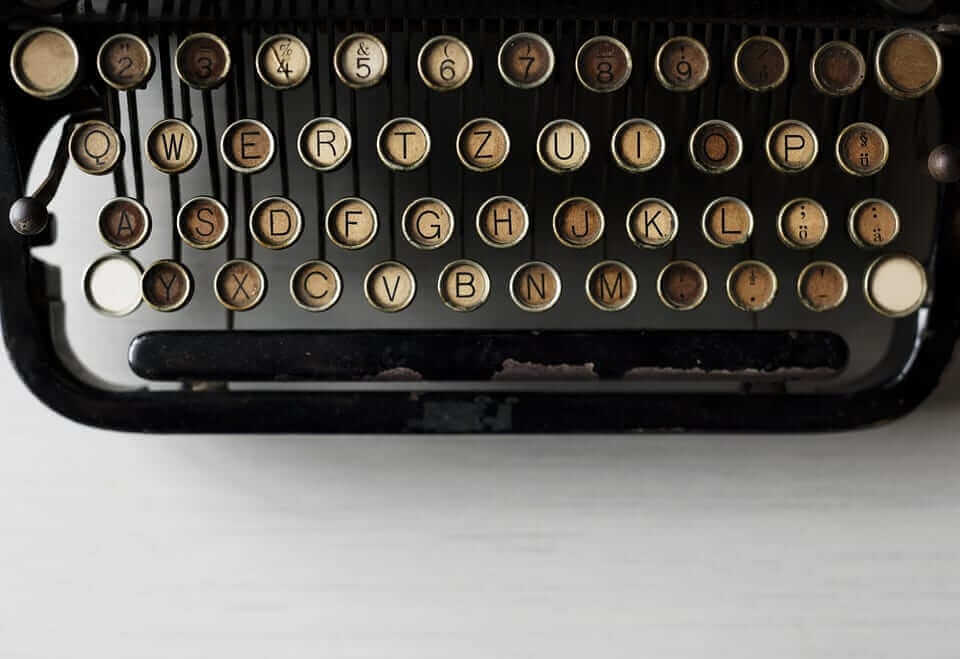 תקריב של מפתחות מכונת כתיבה וינטג מסודרים בארבע שורות. המקשים, מעט בלויים, מציגים אותיות בפריסת QWERTZ, המזכירה את תשומת הלב המוקפדת שהייתם מצפים לה בעת בחירת בחירת חברת תרגום. מספרים וסמלים נשענים על מתכת עגול מיושן ורקע שחור.