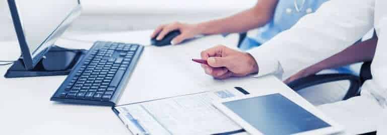 שני אנשים ליד שולחן, האחד משתמש במחשב והשני מצביע על מסמך בעט, כנראה דנים בדברים שכדאי לדעת. ההגדרה כוללת מקלדת, צג וטאבלט, מה שמציע סביבת עבודה שיתופית.