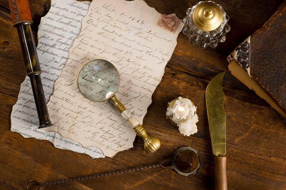 סצנת וינטג על שולחן עץ כוללת אותיות בכתב יד, זכוכית מגדלת, ספר ישן, עט נוצה וטלסקופ פליז - כולם מהדהדים את עושר ההיסטוריה והתרבות. נר על מחזיק דקורטיבי וסכין זהב מקושט משלימים את הטבלה הנוסטלגית.