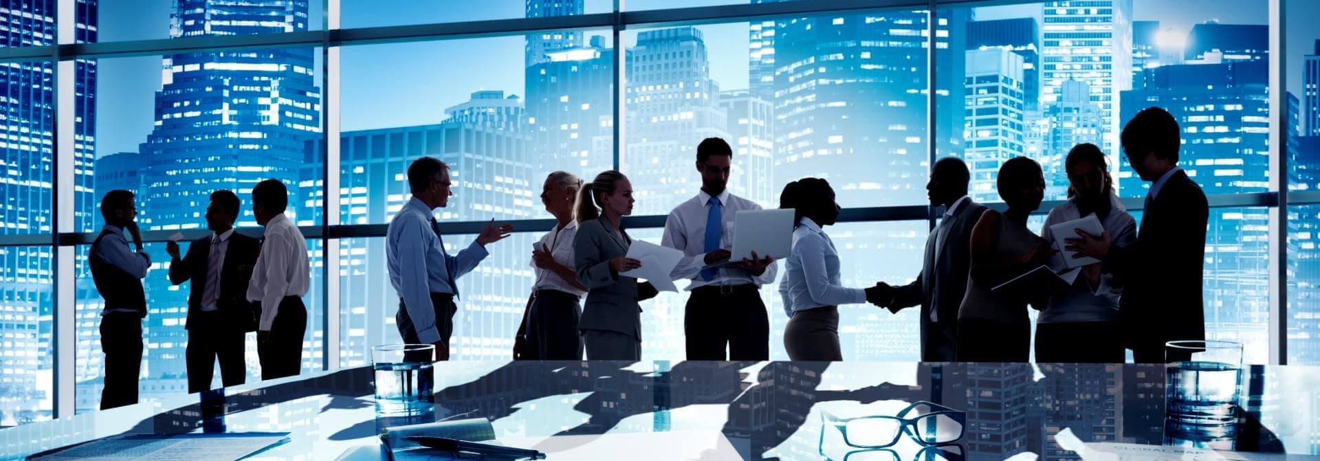 קבוצה של אנשים בלבוש מקצועי עוסקת בישיבת דירקטוריון, דנים ועיון במסמכים במשרד מודרני עם חלונות גדולים. קו הרקיע של העיר נראה ברקע, בנייניה מוארים על רקע שמי דמדומים, כאשר הם שוקלים אפשרויות הקלטה ותמלול.