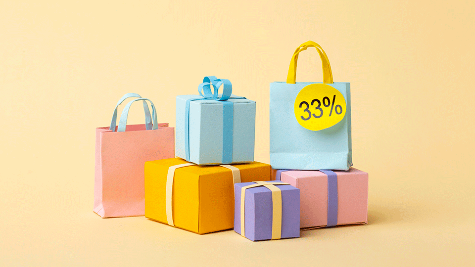 קופסאות מתנה ושקיות מנייר צבעוניים מוערמים על רקע פסטל, משדרים קסם שיווקי. באחד התיקים מופיע עיגול צהוב ועליו כתוב 33%, מרמז על מבצע מפתה. הקופסאות מציגות גוונים של ורוד, צהוב, כחול וסגול.